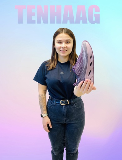 Frau in schwarzer Kleidung und blonden Haaren hat einen Gabor Sneaker in der Hand und zeigt auf diesen. Es ist ein Gabor Sneaker in weiß mit Straßteinen vorne, Bild hat Verlinkung zu dem Schuh im Onlineshop