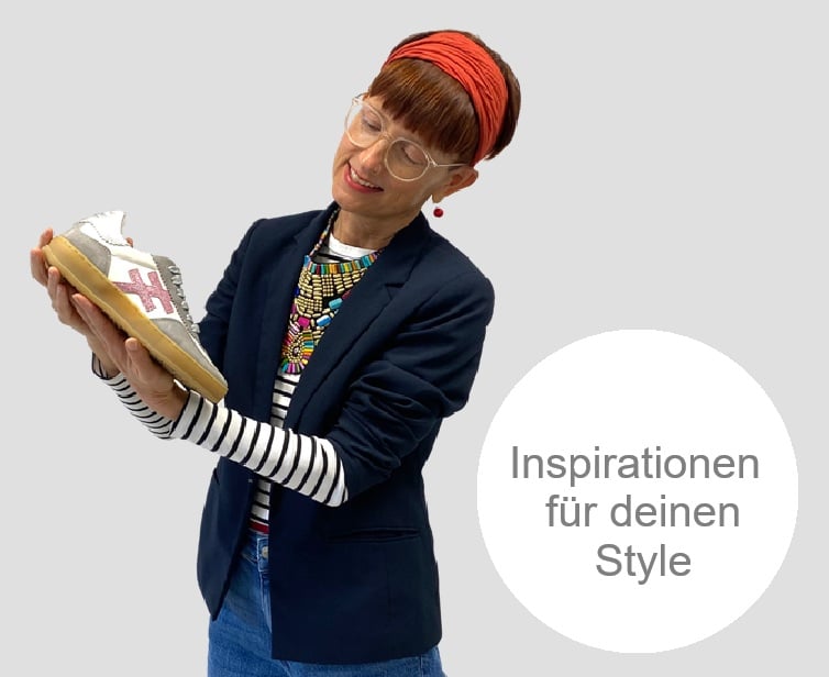 Frau moit einem orangefarbenen Strinband und blauem Jacket Jean und bunter Kette Schaut auf einen Another Trends Schuhe weiße mit lila und silber und gumsohle